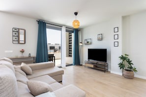 A modern living room with a sofa, TV, and a dining area visible through a glass door. - Home2Book Bright Abades Apt, Pool & Gym (Abades)
