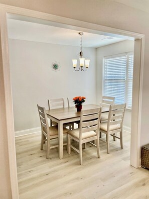 A dining area with a wooden table and chairs, a chandelier, and a window with blinds. - The Cozy Pond House — Spacious, Cozy, Peaceful (Olive Branch)