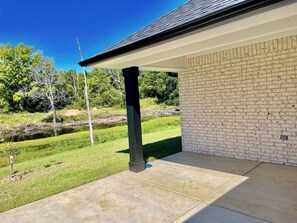 A covered patio area with a brick wall and a concrete floor. - The Cozy Pond House — Spacious, Cozy, Peaceful (Olive Branch)