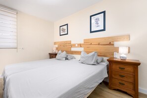 A hotel room with a large bed, wooden headboard, two bedside tables with lamps, and two framed pictures on the wall. - Home2Book Morro Jable Coastal Studio by the Beach (Solana Matorral)