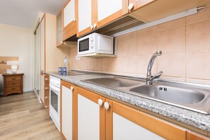 A kitchen with wooden cabinets, a stainless steel sink, a microwave, and a countertop with a water bottle and cups. - Home2Book Morro Jable Coastal Studio by the Beach (Solana Matorral)