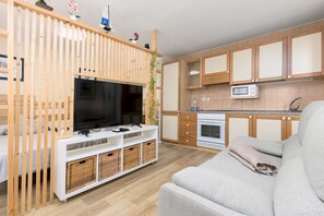 A modern kitchen with a built-in microwave, oven, and a wooden TV stand with a flat-screen TV. - Home2Book Morro Jable Coastal Studio by the Beach (Solana Matorral)