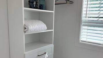 A white closet with shelves, a hanging rack, and a window with blinds.