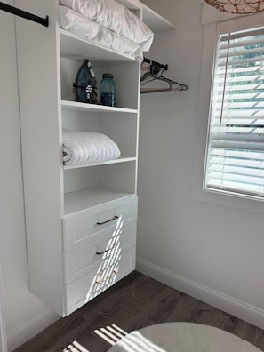A white closet with shelves, a hanging rack, and a window with blinds. - Private Downtown Bluffton Carriage House (Bluffton)