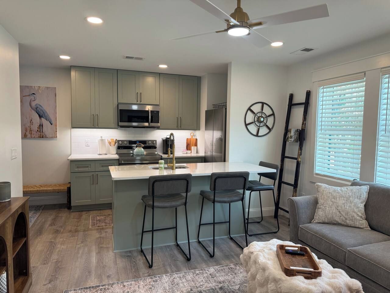 A modern kitchen with a central island, bar stools, and a dining area with a sofa and a coffee table.