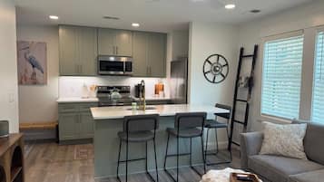 A modern kitchen with a central island, bar stools, and a dining area with a sofa and a coffee table.