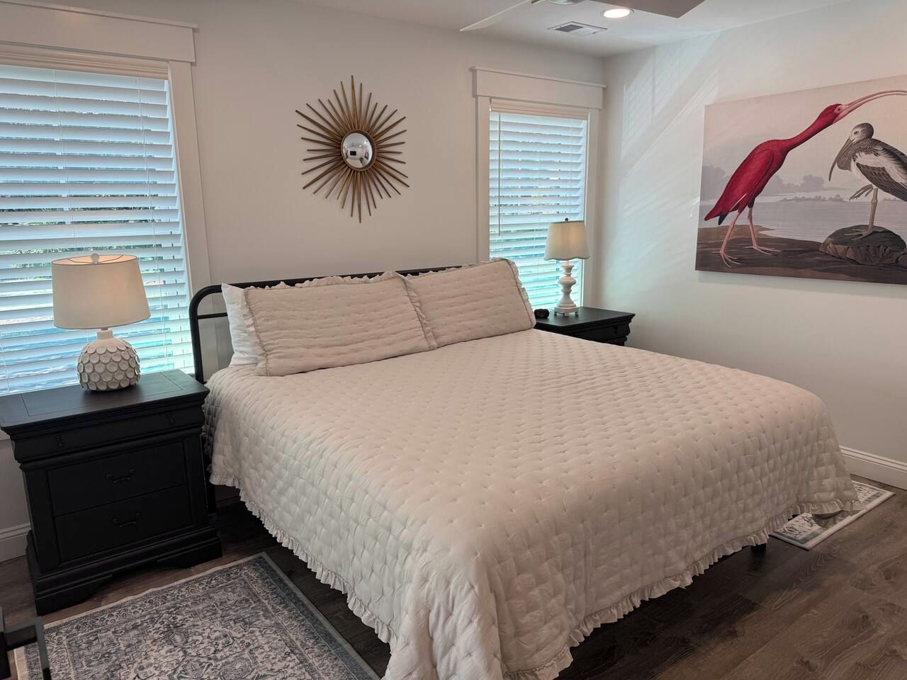 A bedroom with a bed, nightstands, a lamp, a wall clock, and a painting.