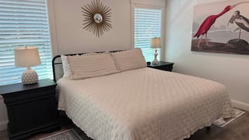 A bedroom with a bed, nightstands, a lamp, a wall clock, and a painting.