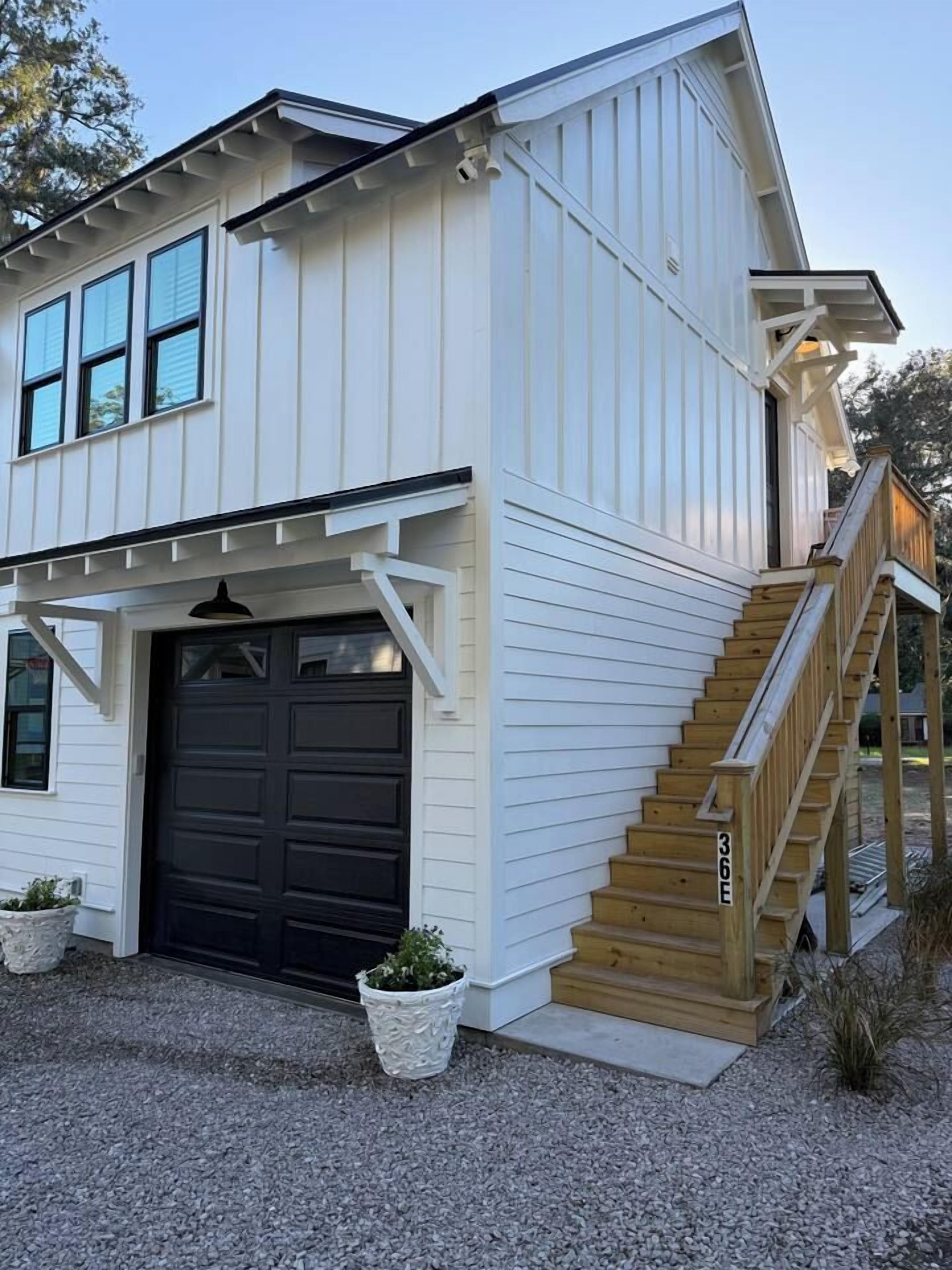 A two-story house with a dark garage door, a wooden staircase, and a gravel driveway.