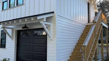 A two-story house with a dark garage door, a wooden staircase, and a gravel driveway.