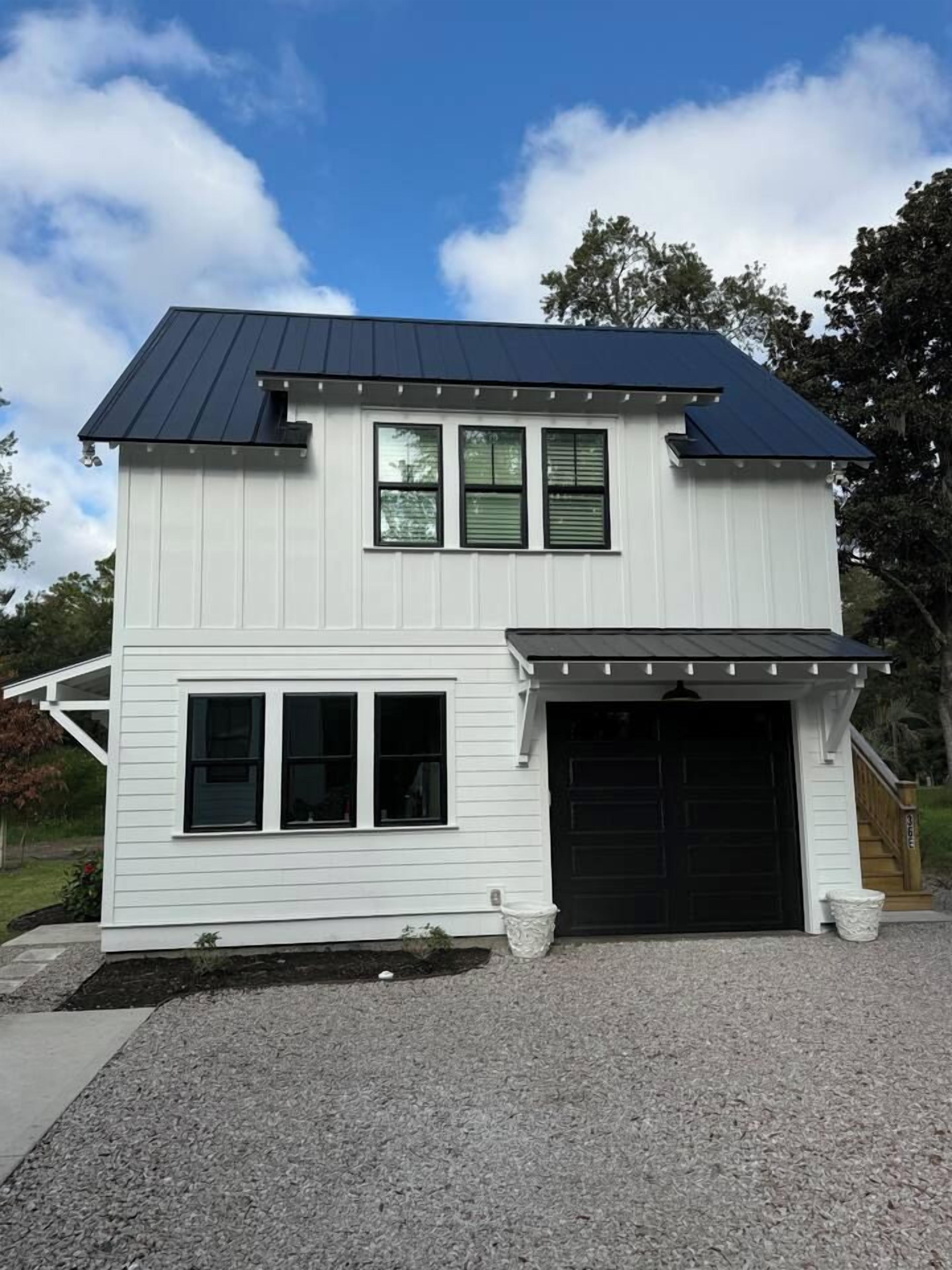 Une maison à deux étages avec un garage, une véranda et une allée gravillonnée.