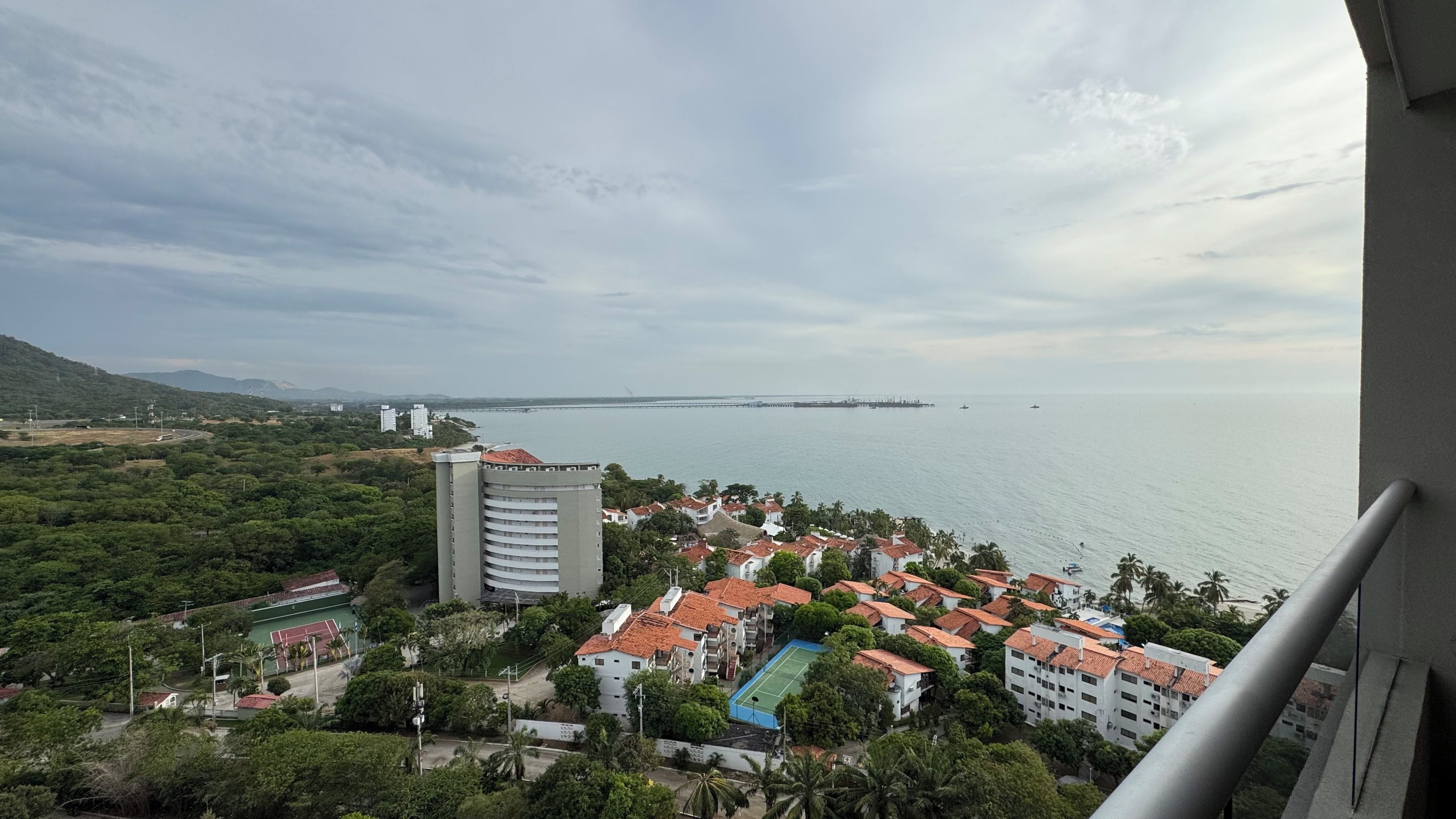 Una zona residencial costera con vistas al mar, un edificio grande y una cancha de tenis.