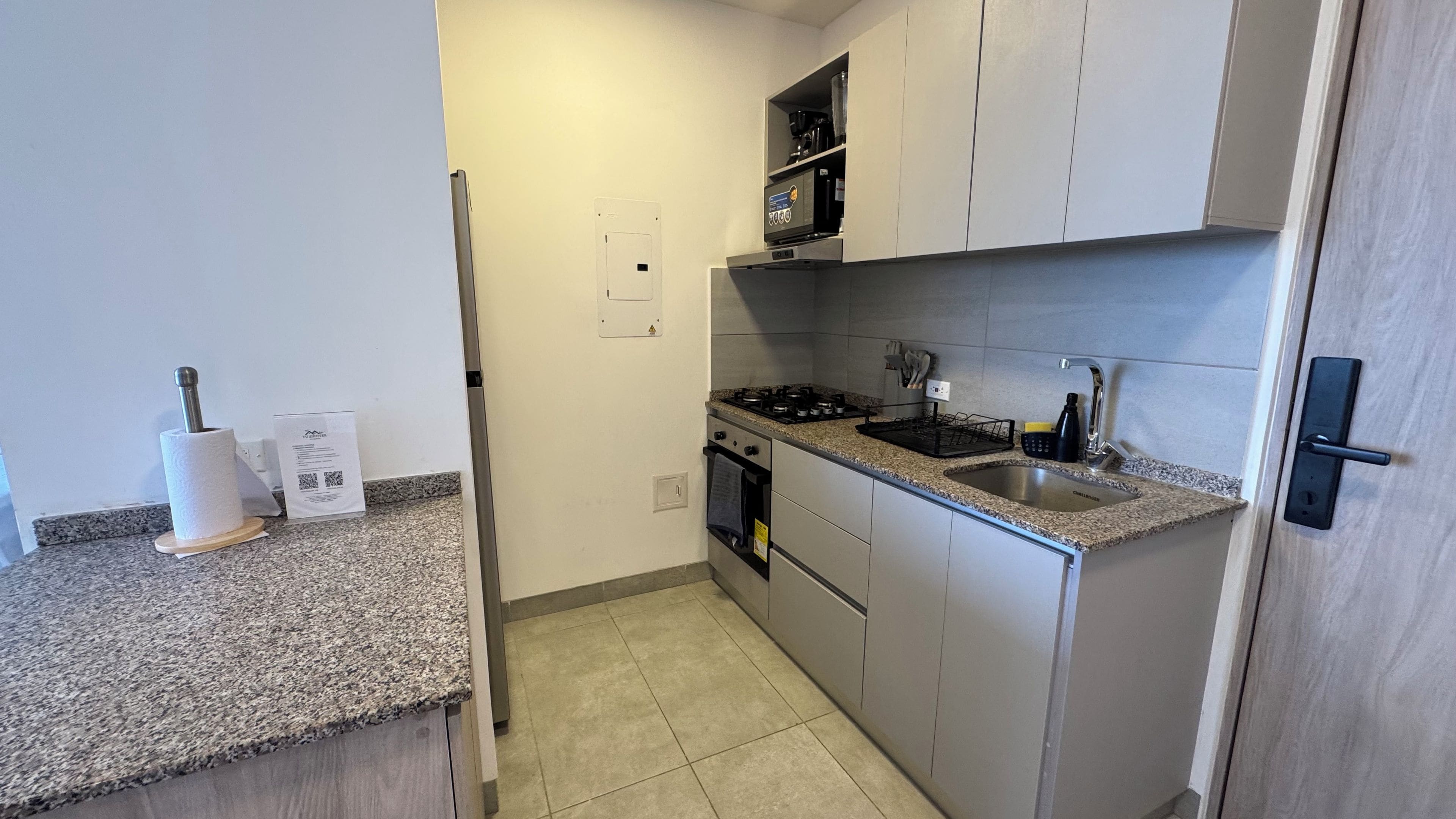 Una cocina compacta con estufa a gas, microondas integrado y pileta de acero inoxidable.