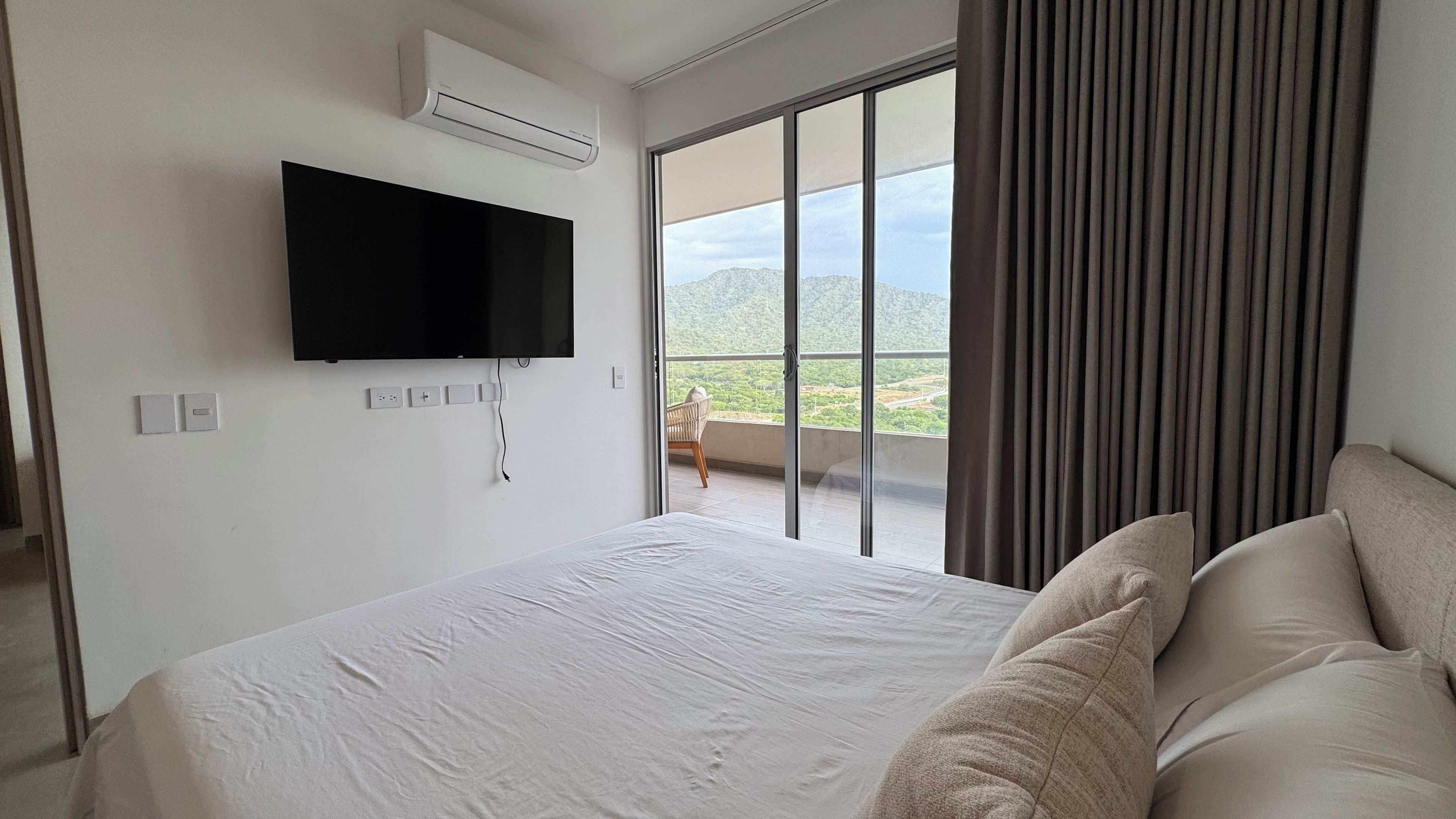 Une chambre d’hôtel avec un lit, un téléviseur à écran plat fixé au mur et une vue sur un balcon équipé d’une chaise.
