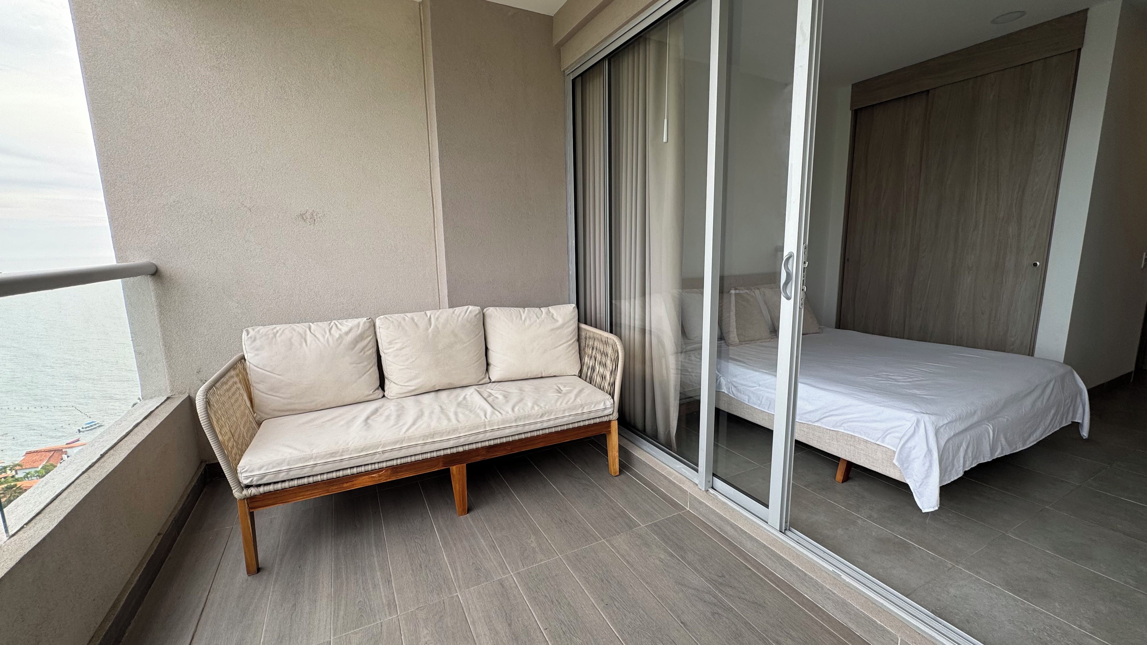 Un balcon avec un canapé et un lit, une porte-fenêtre coulissante et une vue sur la mer.