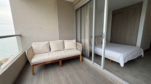 Un balcon avec un canapé et un lit, une porte-fenêtre coulissante et une vue sur la mer.
