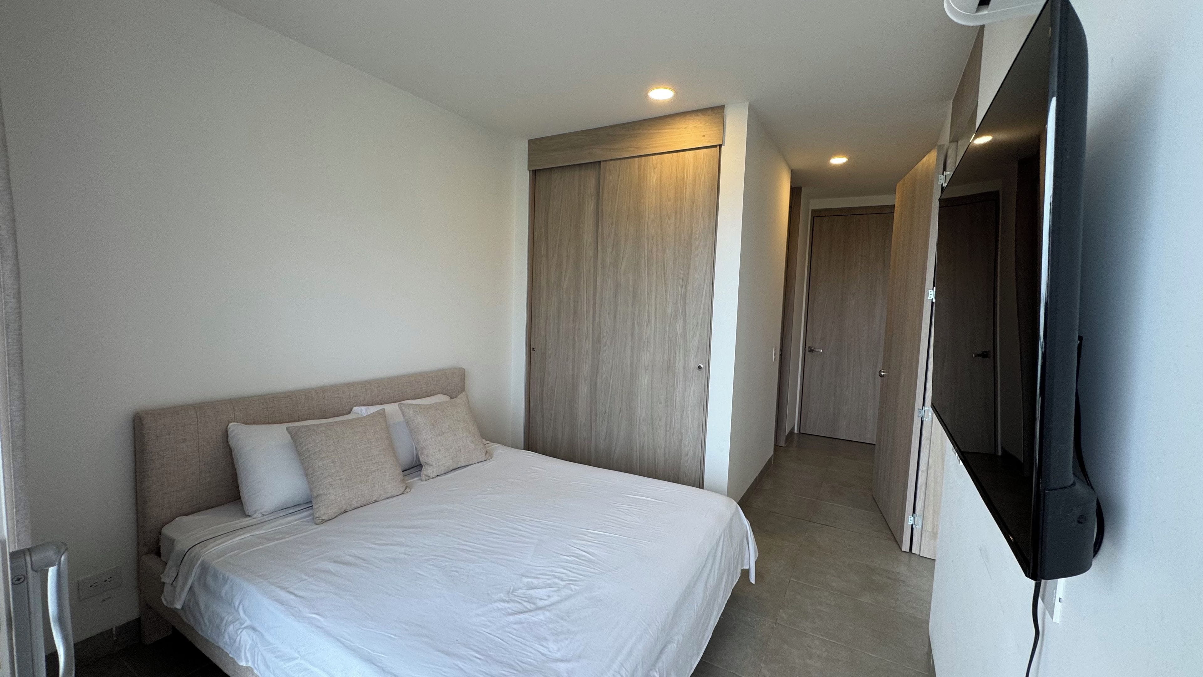 Una habitación de hotel con una cama, un armario y un televisor montado en la pared.