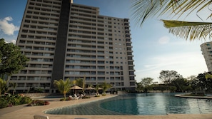 Un hotel de gran altura con piscina, palmeras y sillones de descanso.