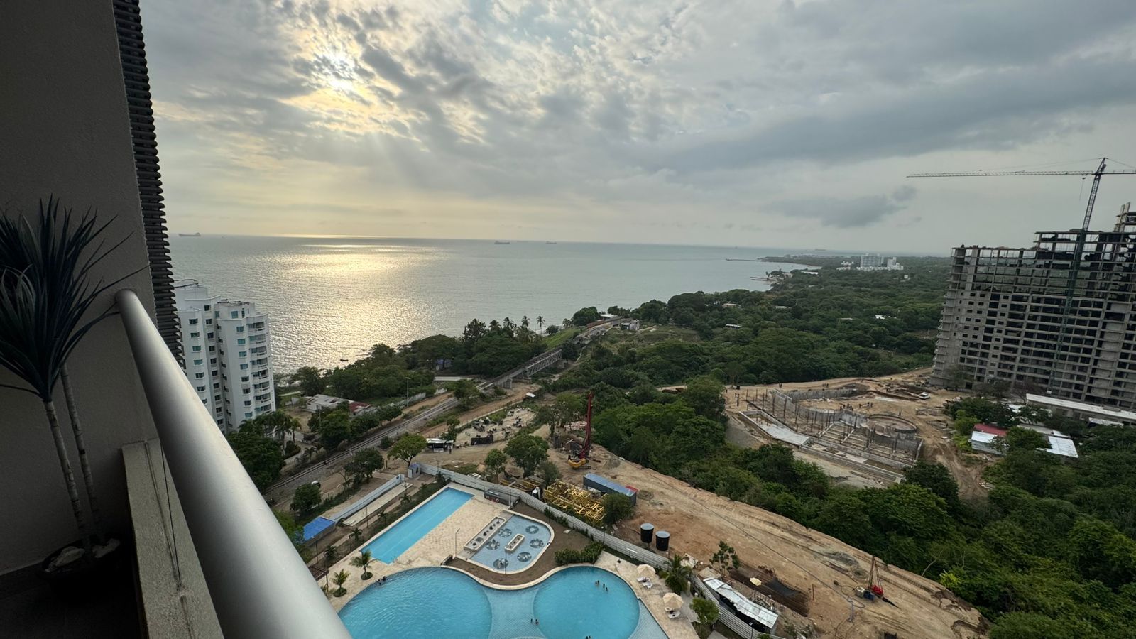 Vista de una piscina con vistas al mar y una obra en construcción al fondo.