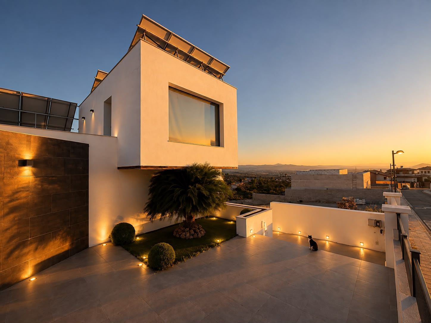 Uma casa moderna de dois andares com telhado plano, janelas amplas e área externa bem iluminada, com um pequeno jardim e um gato.