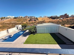 Une terrasse sur le toit avec une piscine, une petite pelouse et une vue sur les maisons environnantes.