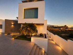 A modern house with a flat roof, a large window, and a staircase leading to the entrance.