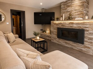 A modern living room with a beige sofa, a flat-screen TV, a stone fireplace, and a small table with a candle. - Villa Quesada - A villa where you can unwind. (AN)