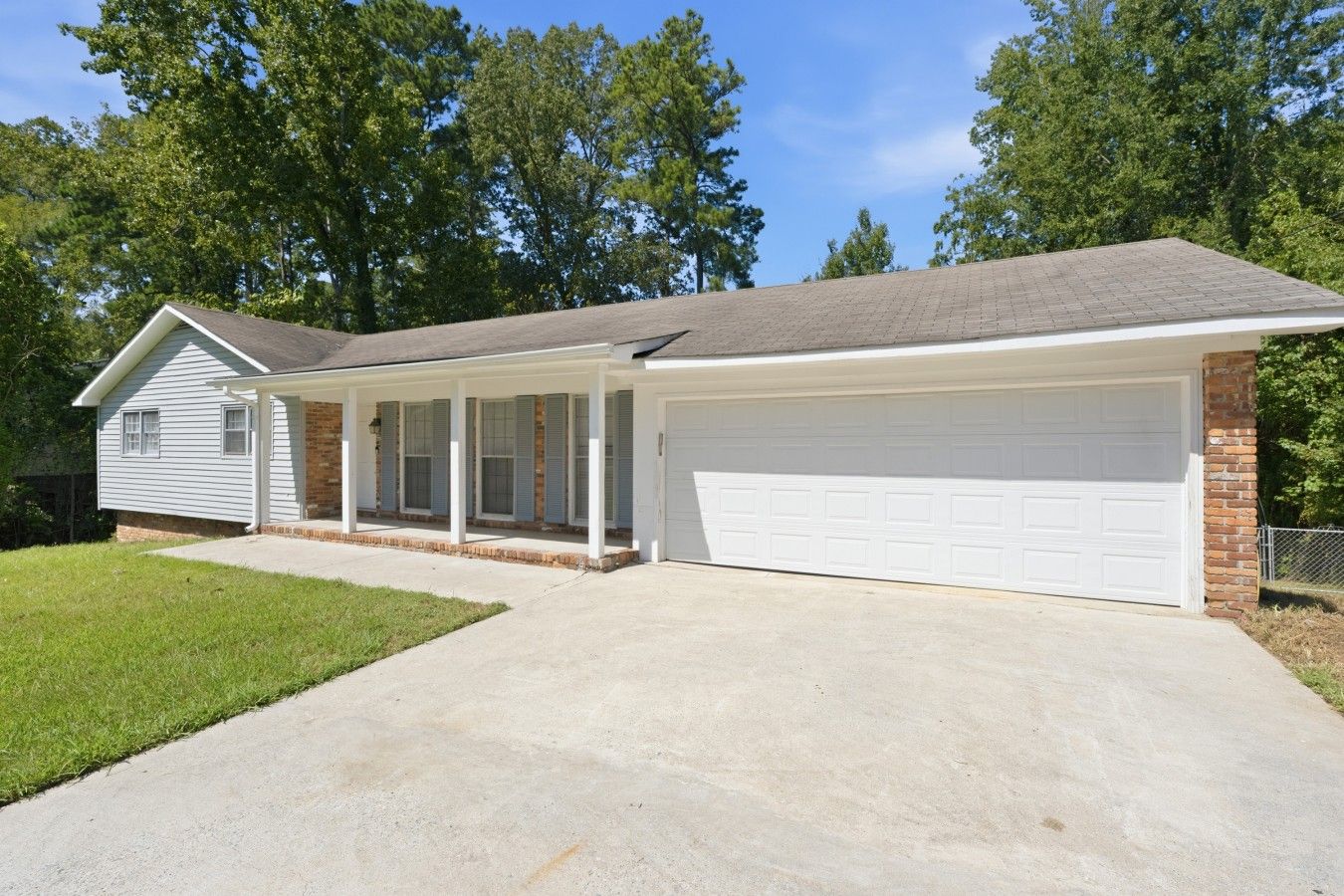 Ein Bungalow mit überdachter Veranda, Garage und gepflegtem Rasen.