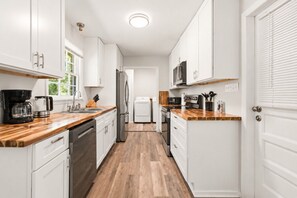 Una cucina moderna con mobili bianchi, piani in legno, elettrodomestici in acciaio inossidabile e un'isola centrale.