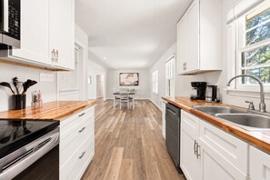 Una cocina moderna con armarios blancos, encimeras de madera, lavavajillas y cafetera.