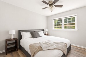 Camera da letto con un letto, due comodini, una ventola a soffitto, una finestra e vista sul verde.