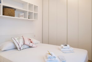 A neatly made bed with pillows, a shelf above with a basket and a framed picture, and towels and toiletries on the bed. - Milano Zara Urban Nest (Milan)