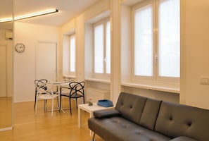 A modern living room with a sofa, a dining table with chairs, and a window with blinds. - Milano Zara Urban Nest (Milan)