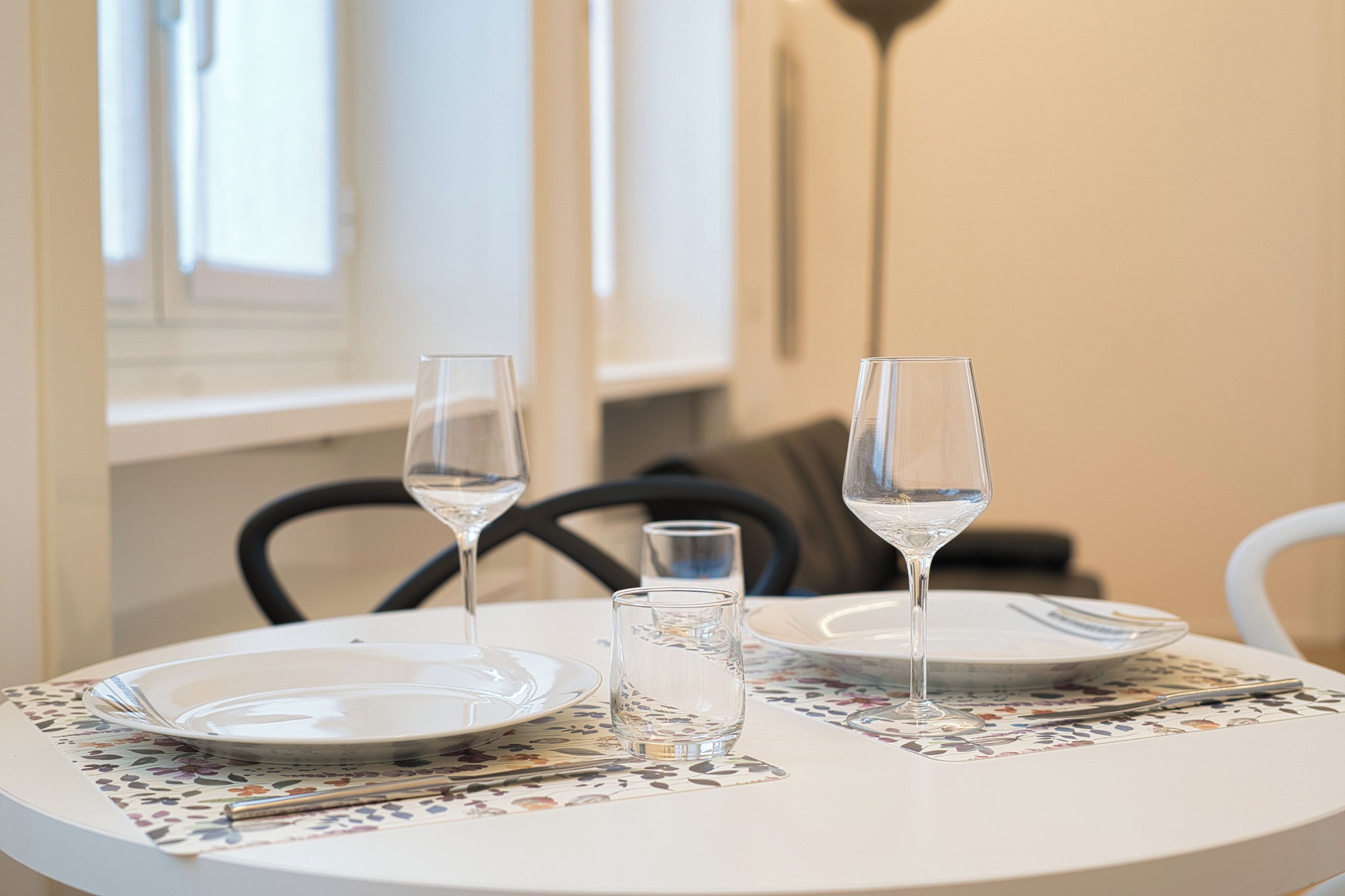 A dining table with two wine glasses, a water glass, and a plate set with cutlery.