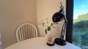 Et bord med en hvid stol, en sort skrivebordslampe, en hvid vase med en plante og en Buddha-figur.