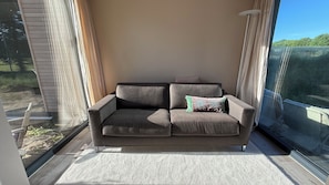 En grå sofa med et mønstret pude i et hjørne af et rum med et stort vindue.