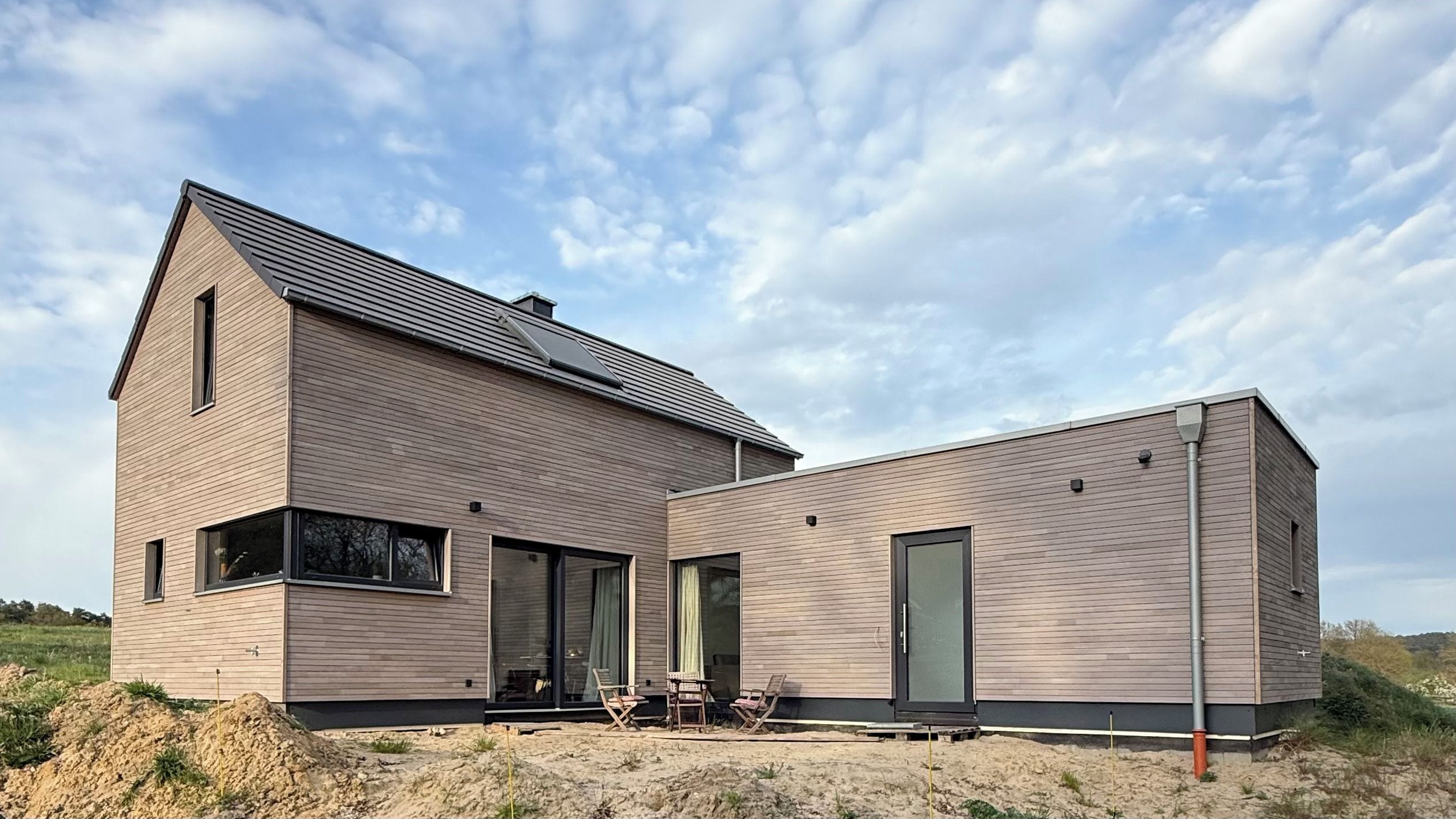 Una casa moderna de dos pisos con techo plano, ventanas amplias y un paisaje arenoso.