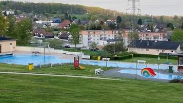 Una piscina con una torre de salvavidas y un mural de arcoíris, rodeada de césped y edificios residenciales al fondo.