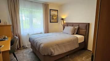 Una habitación de hotel con cama, escritorio, silla, ventana con cortinas y una lámpara en el techo.