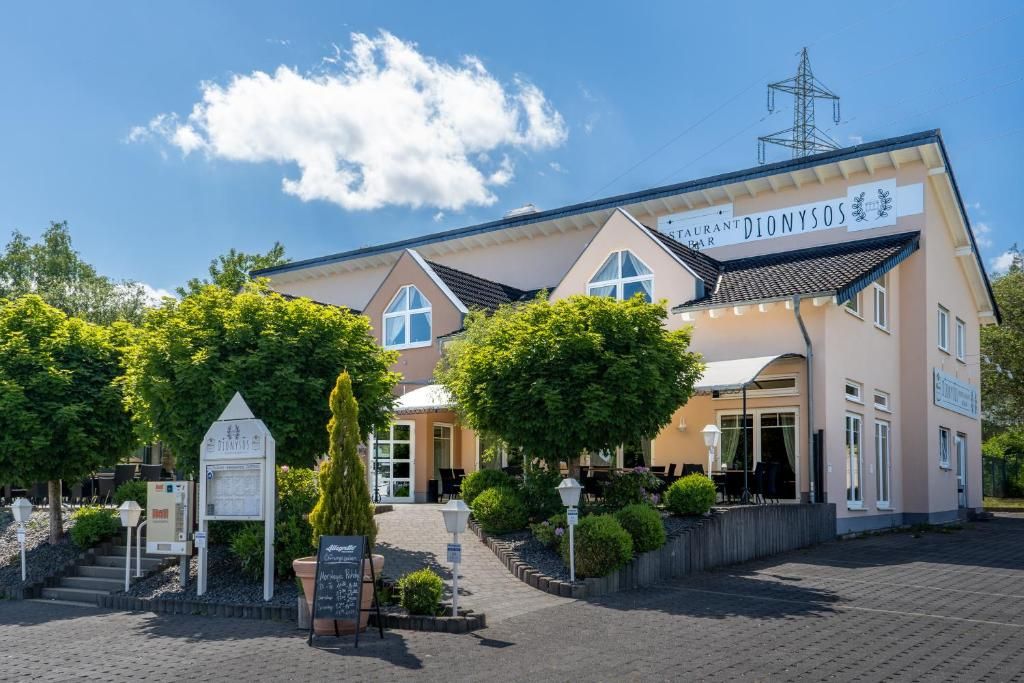 Un hotel con un letrero que dice 'DIONYSOS' y un espacio exterior bien cuidado con árboles y un sendero pavimentado.