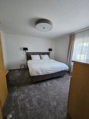 Habitación de hotel con cama, una mesita, lámpara y ventana con cortinas.