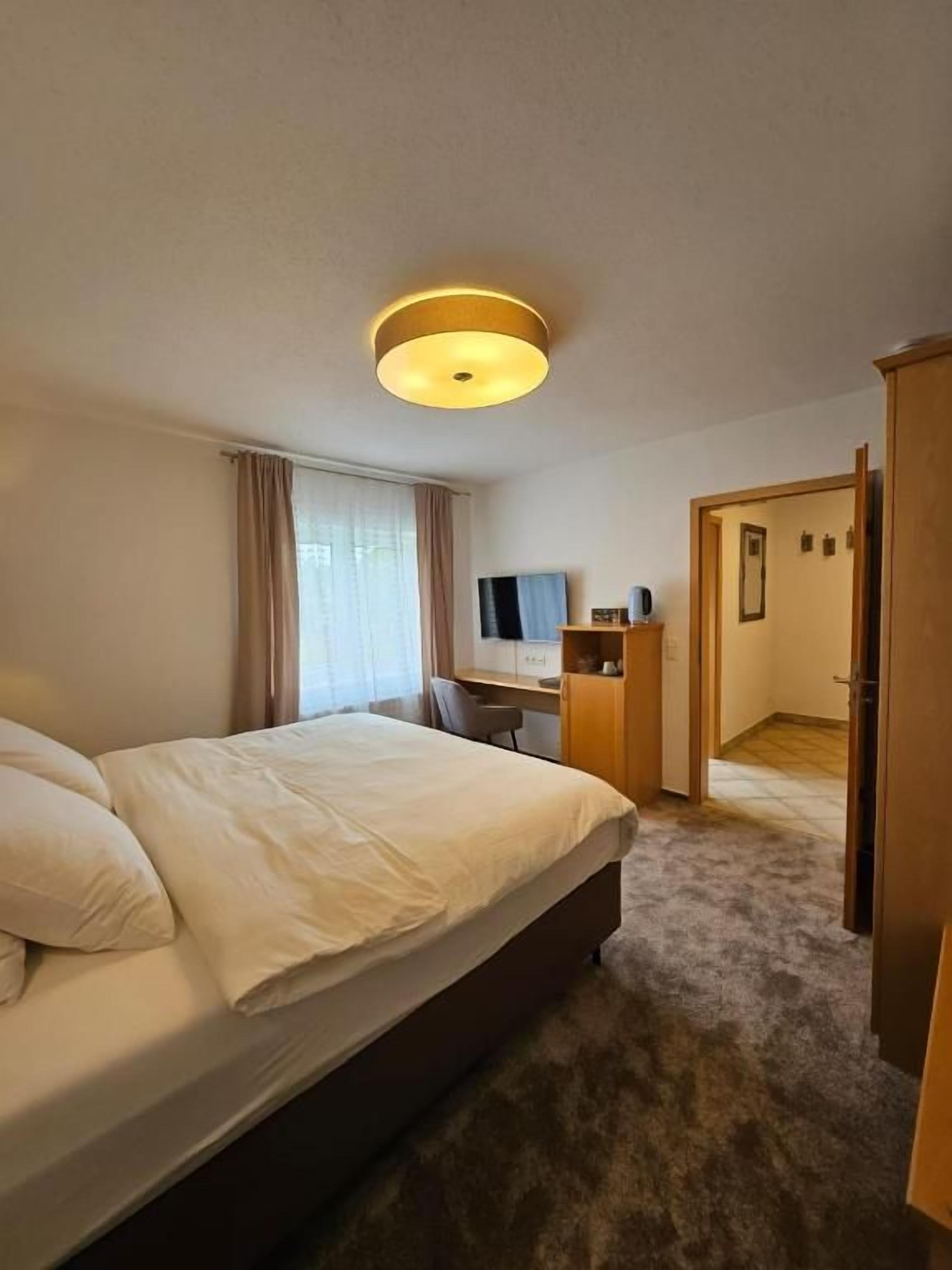 A hotel room with a bed, a desk, a television, and a door leading to another room.