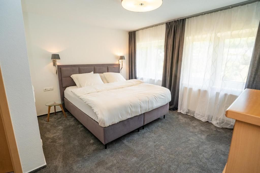Ein Schlafzimmer mit einem Bett, zwei Nachttischlampen, einem kleinen Tisch und einem Fenster mit Vorhängen.