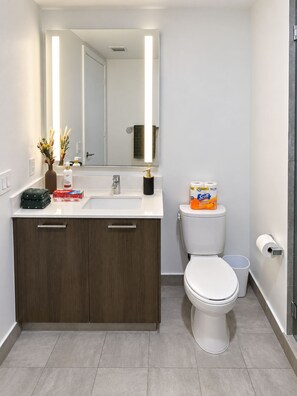 Ein modernes Badezimmer mit einem weißen Waschbecken, dunklen Holzschränken, einer weißen Toilette und einem Spiegel mit integrierter Beleuchtung.