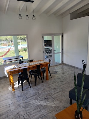 A spacious room with a dining table, chairs, a potted plant, and a sliding glass door leading to an outdoor area. - El Caldén Complex (San Luis)