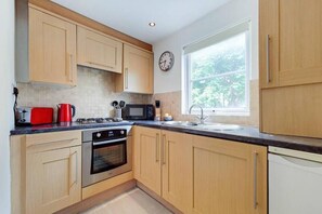 A kitchen with wooden cabinets, a stove, a microwave, and a sink. - AR1 - 1 Bed Apartment in Heart of Fulham (London)