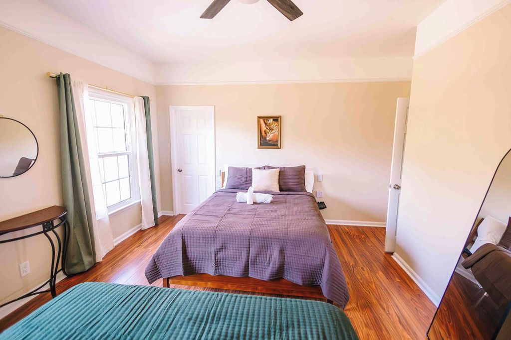 A bedroom with a bed, a bedside table, a chair, a window with curtains, and a door.