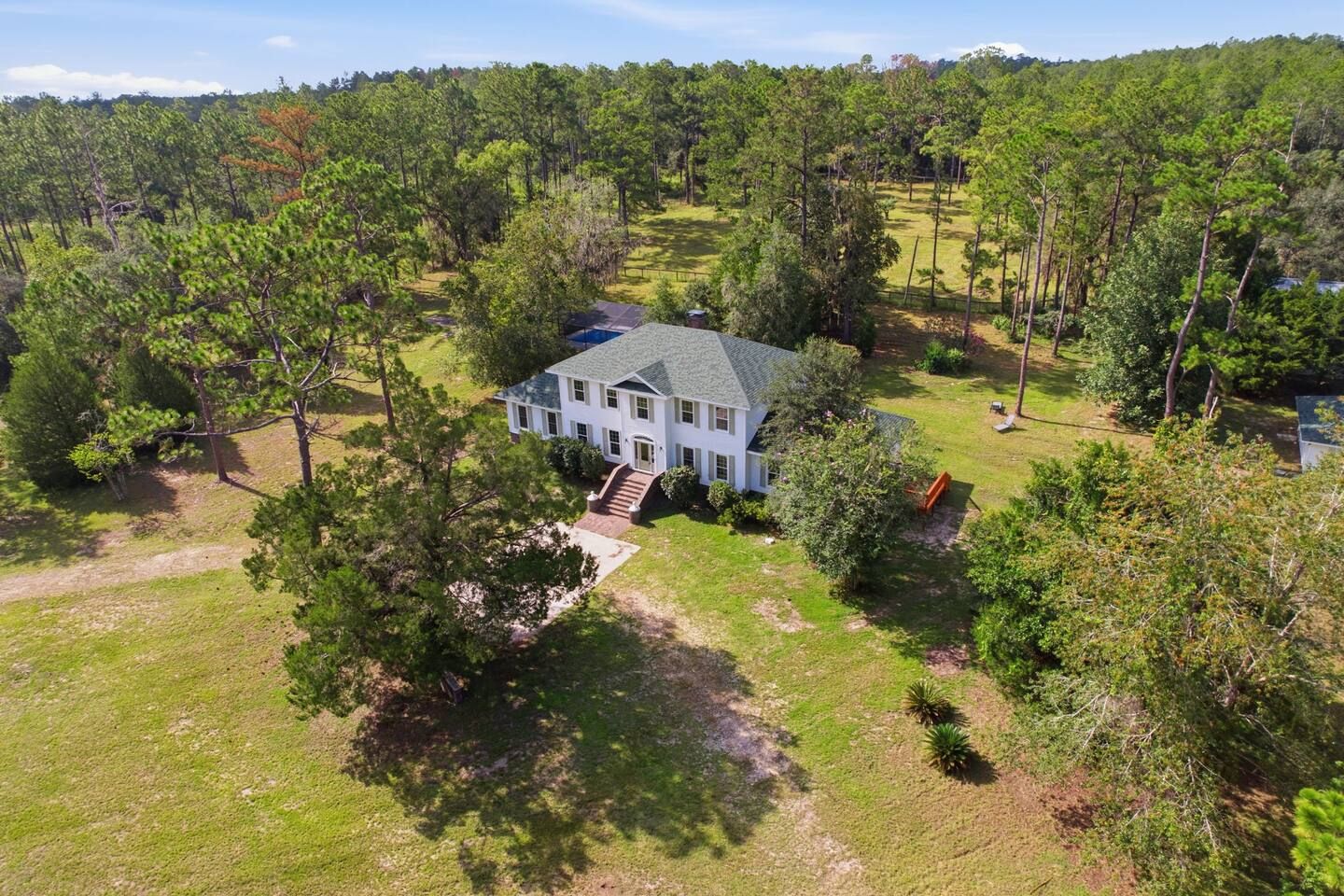 A large white house with a grey roof surrounded by dense trees and a grassy yard.