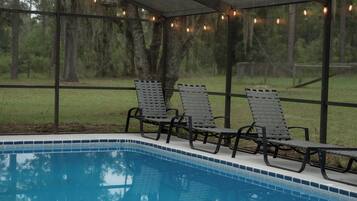 A covered pool area with lounge chairs and string lights.