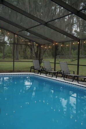 A covered pool area with lounge chairs and string lights.